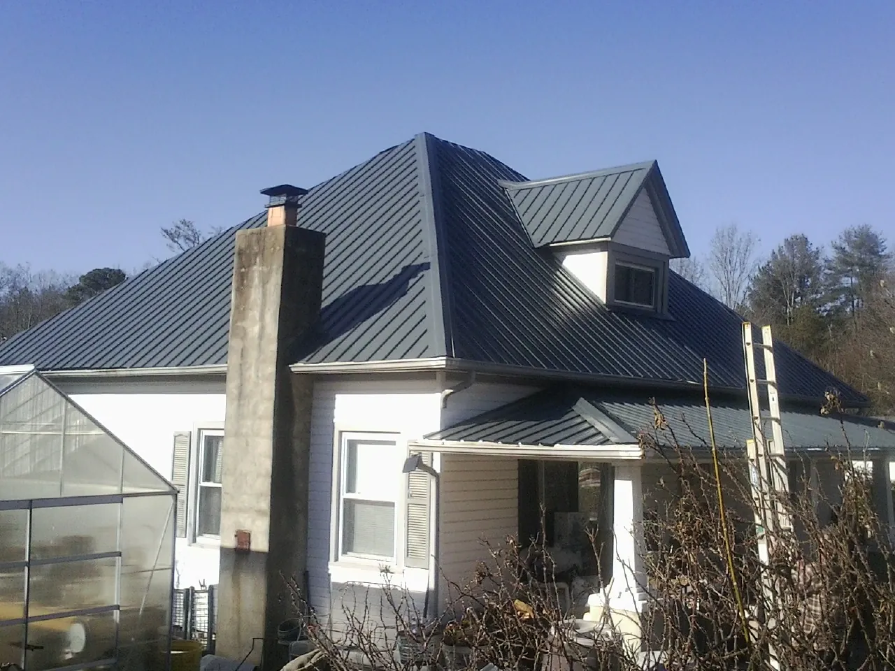 Dark blue standing seam metal roof on a white farmhouse with dormer — Slate & Tile Roof Repair by Roofing Brothers in Wolcott