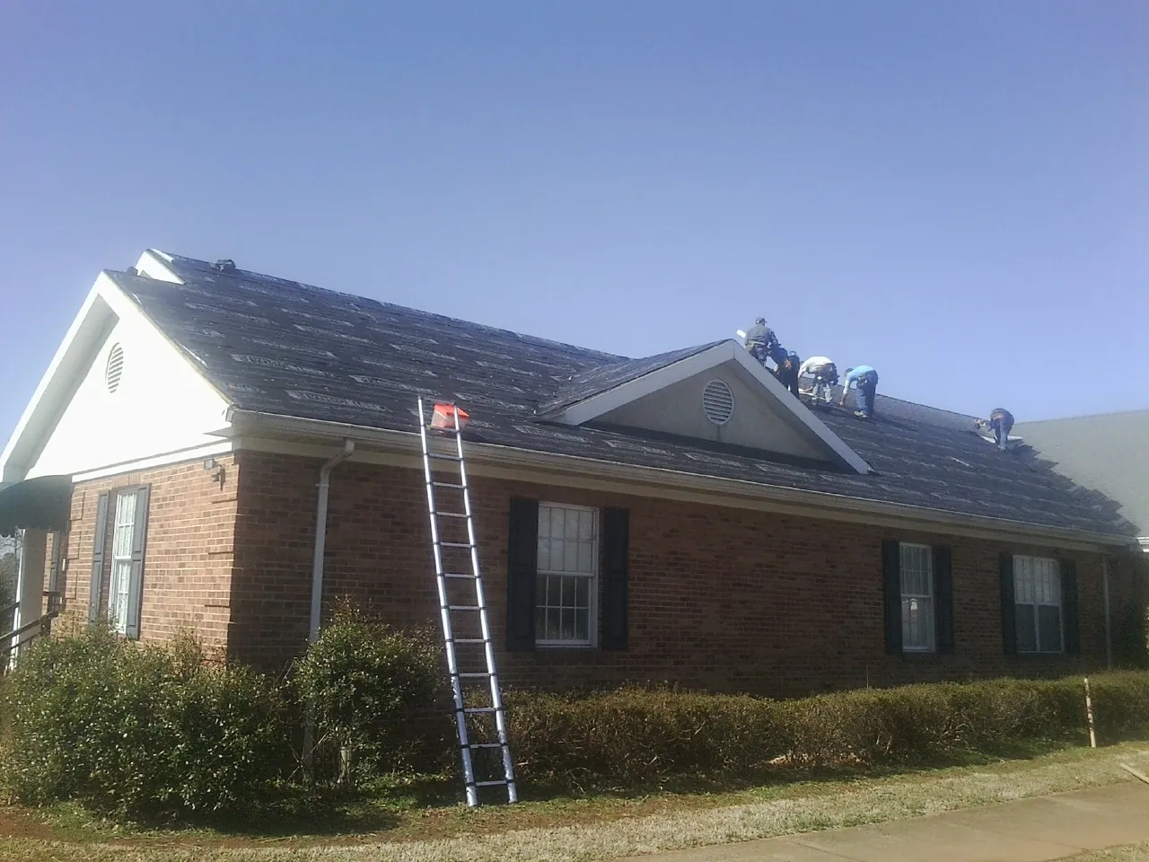 Crew tearing shingles off a brick ranch roof with a ladder set — Emergency Roof Repair work by our crew in Wolcott