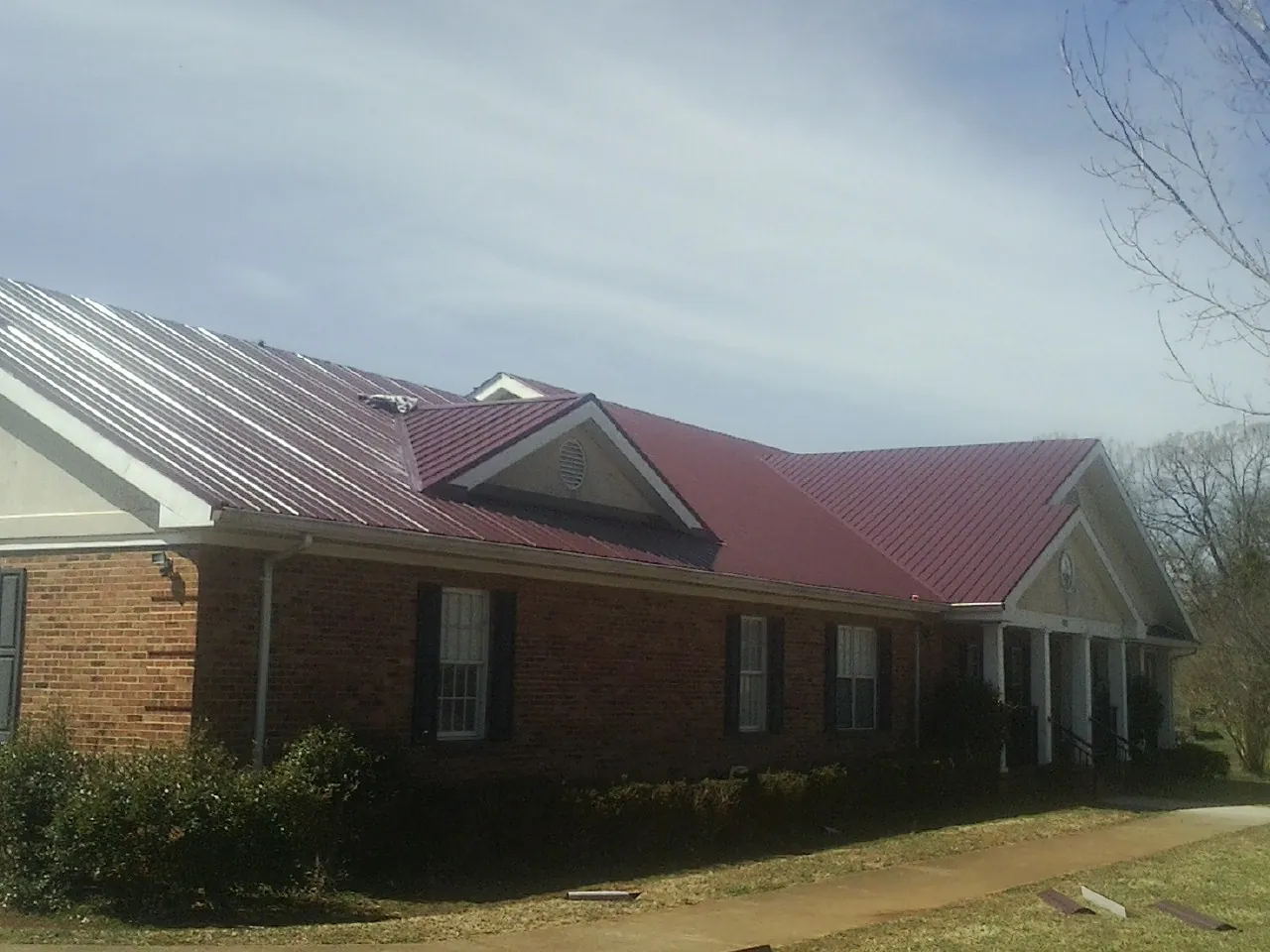 Red metal roof with gabled entries on a long brick building, from a Hail Damage Roof Repair job in Wolcott