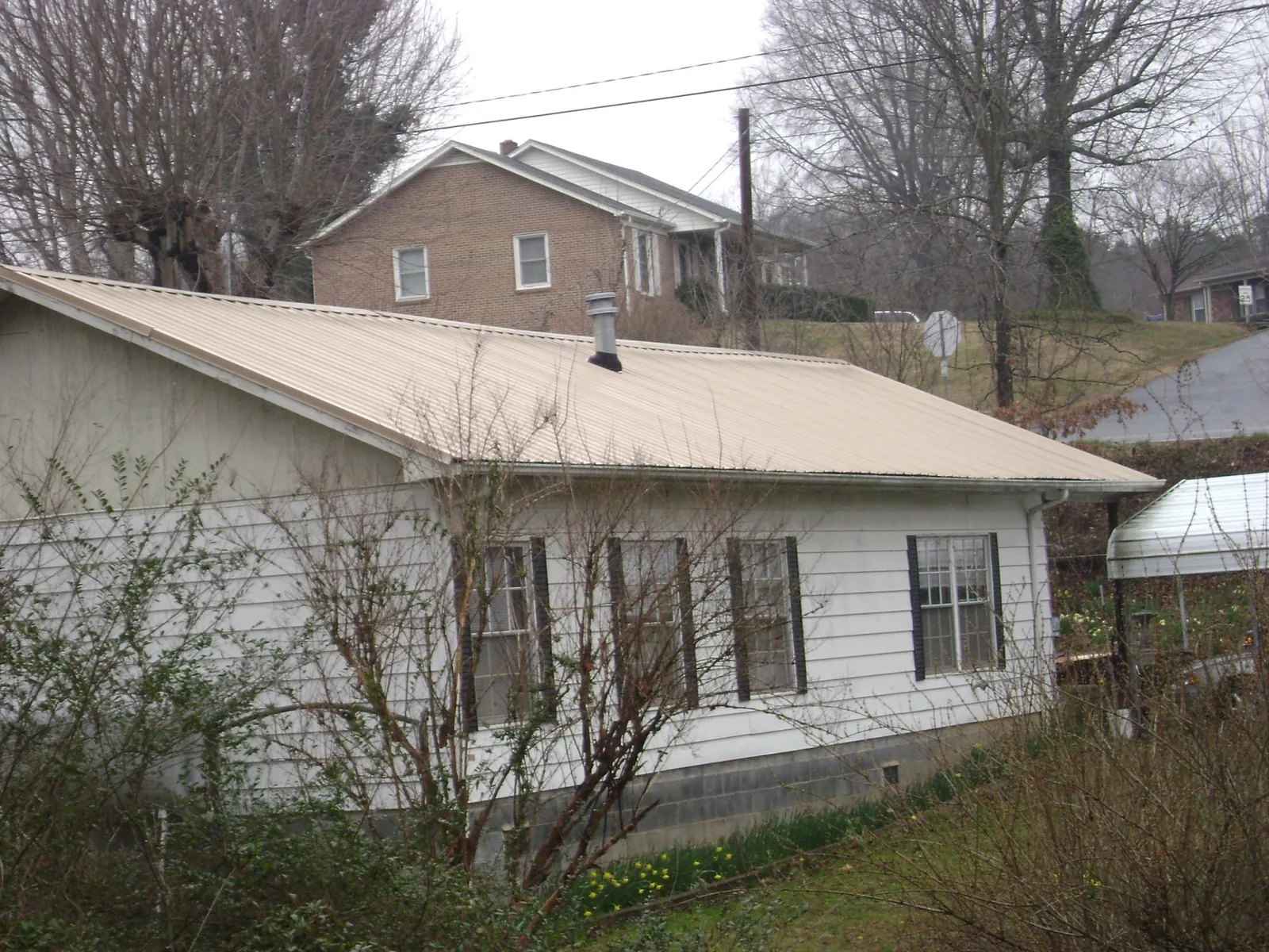 Tan metal roof on a white sided house set into a hillside — Commercial Roofing by Roofing Brothers in Wolcott